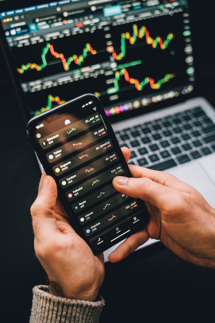A phone showing a stock app in front of a laptop with charts.