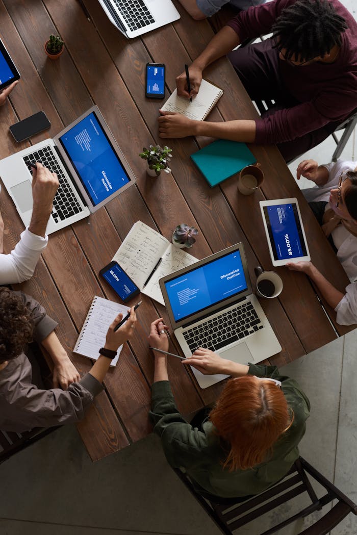 People working around a wooden table with laptops and notebooks.